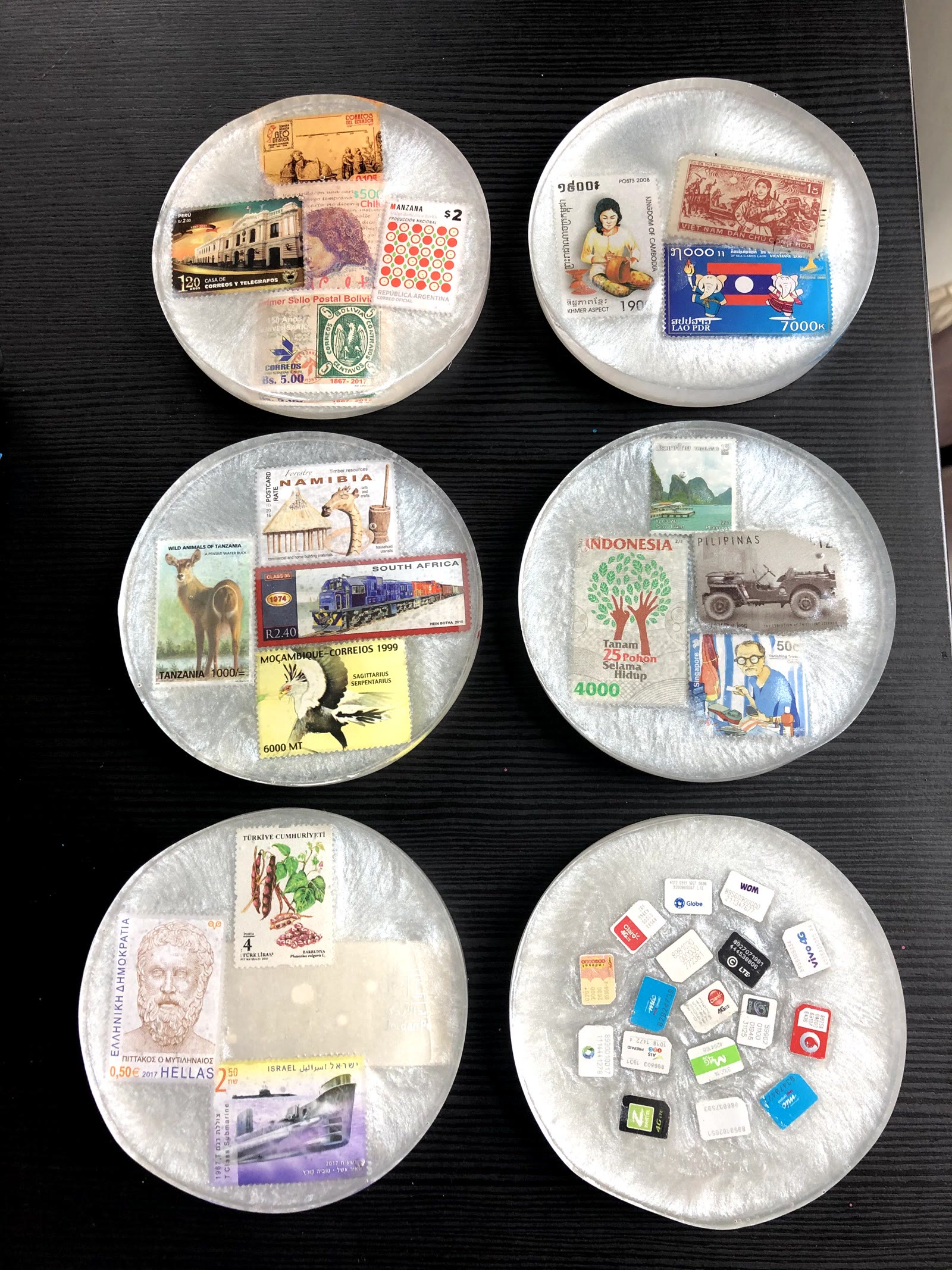 Five round resin coasters holding postage stamps from South America, Southeast Asia, Africa and Europe, plus one round coaster filled with SIM cards