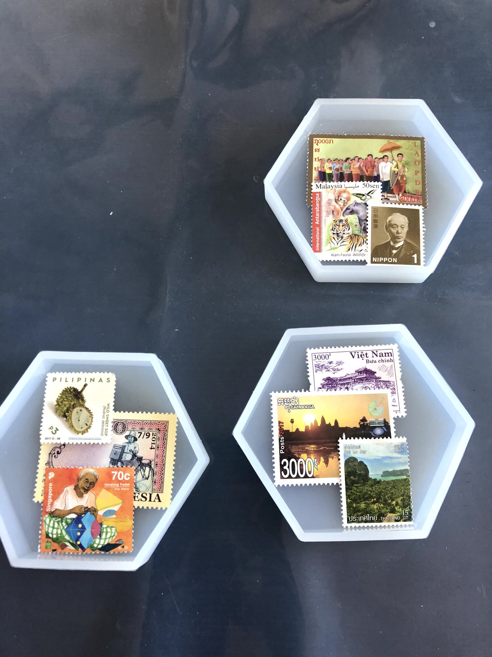 Three hexagon silicone molds each holding three or four postage stamps from Laos, Malaysia, Japan, the Philippines, Indonesia, Singapore, Vietnam, Cambodia and Thailand, before the resin is poured