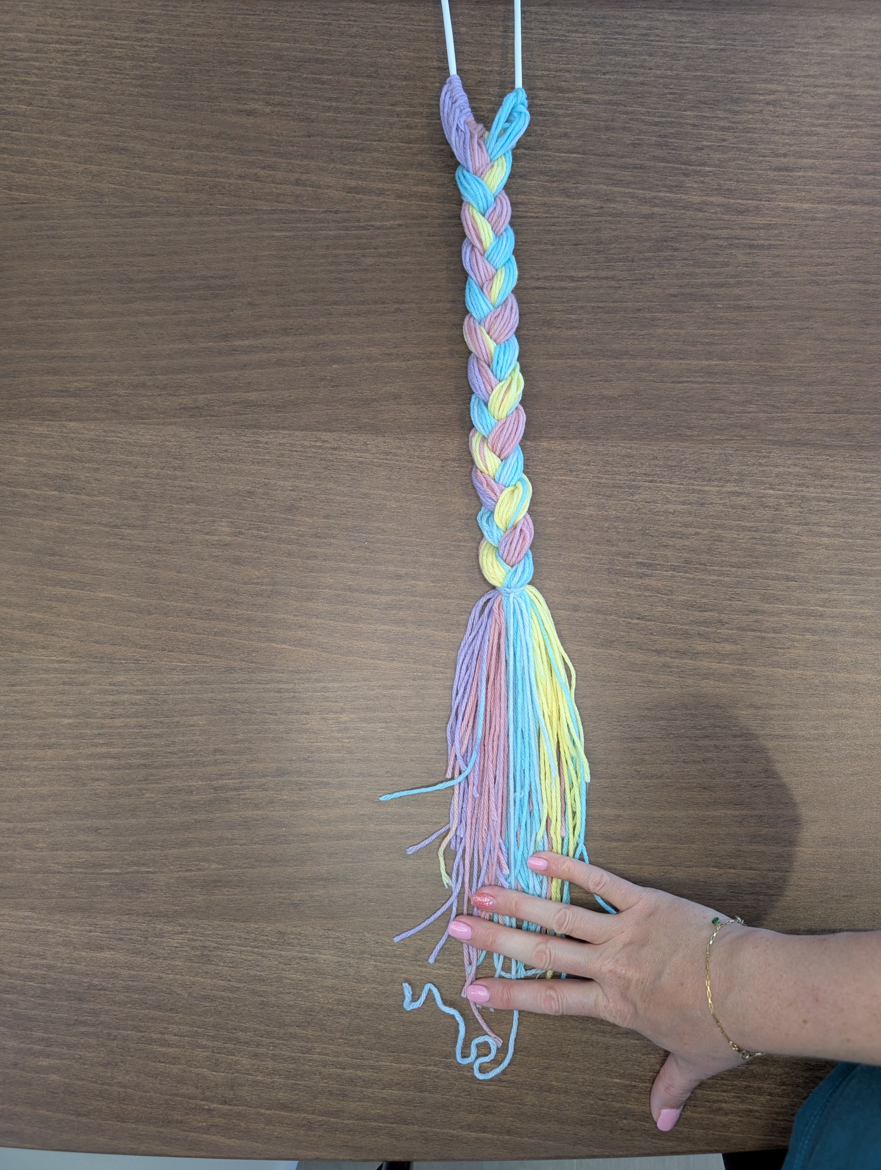 Braided rainbow yarn tail with the ends tied off and the strands still loose and uneven, with a hand for scale