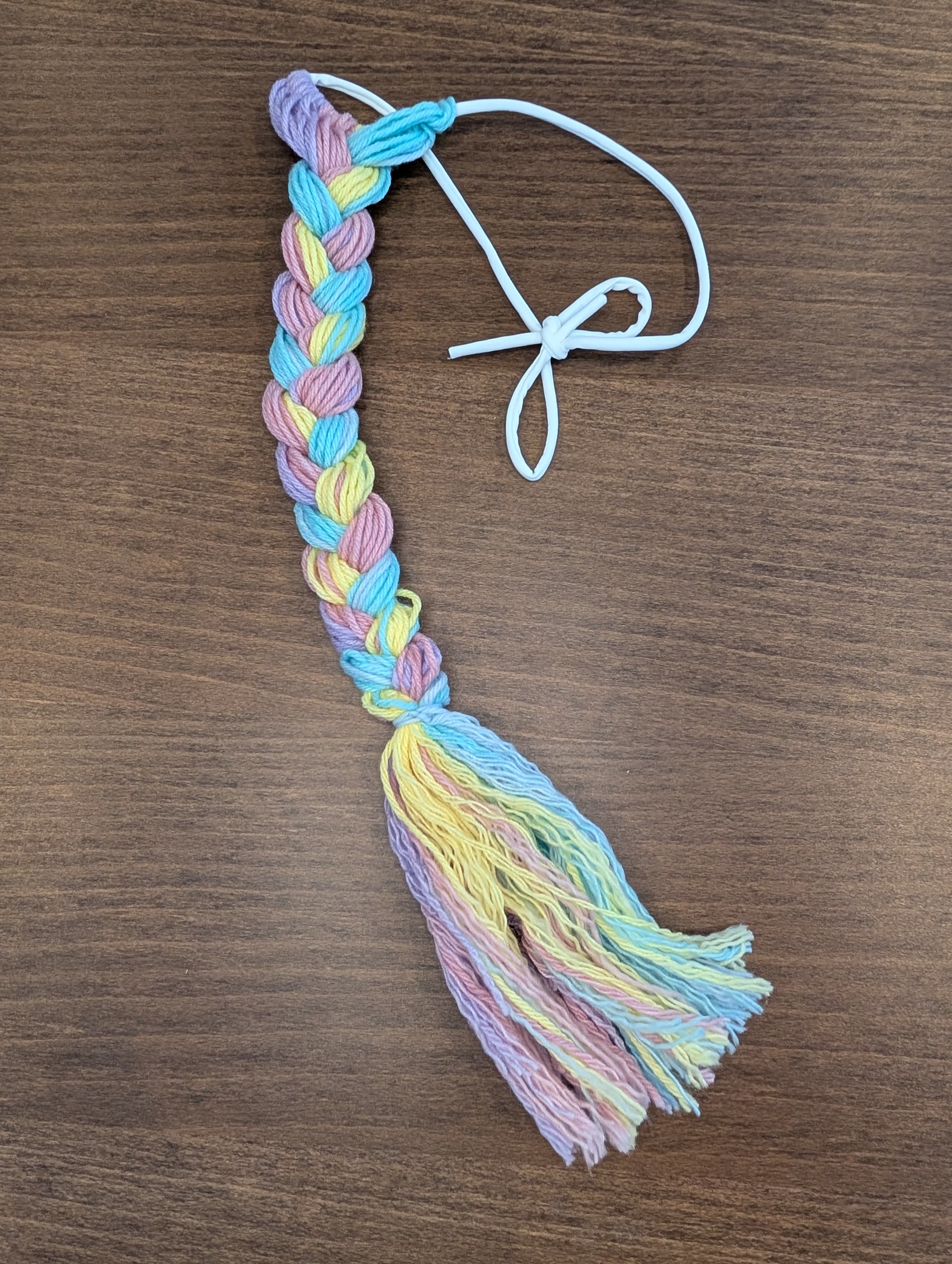 Finished braided pastel rainbow yarn tail with a fluffy brushed-out end and a white elastic waistband tied in a bow