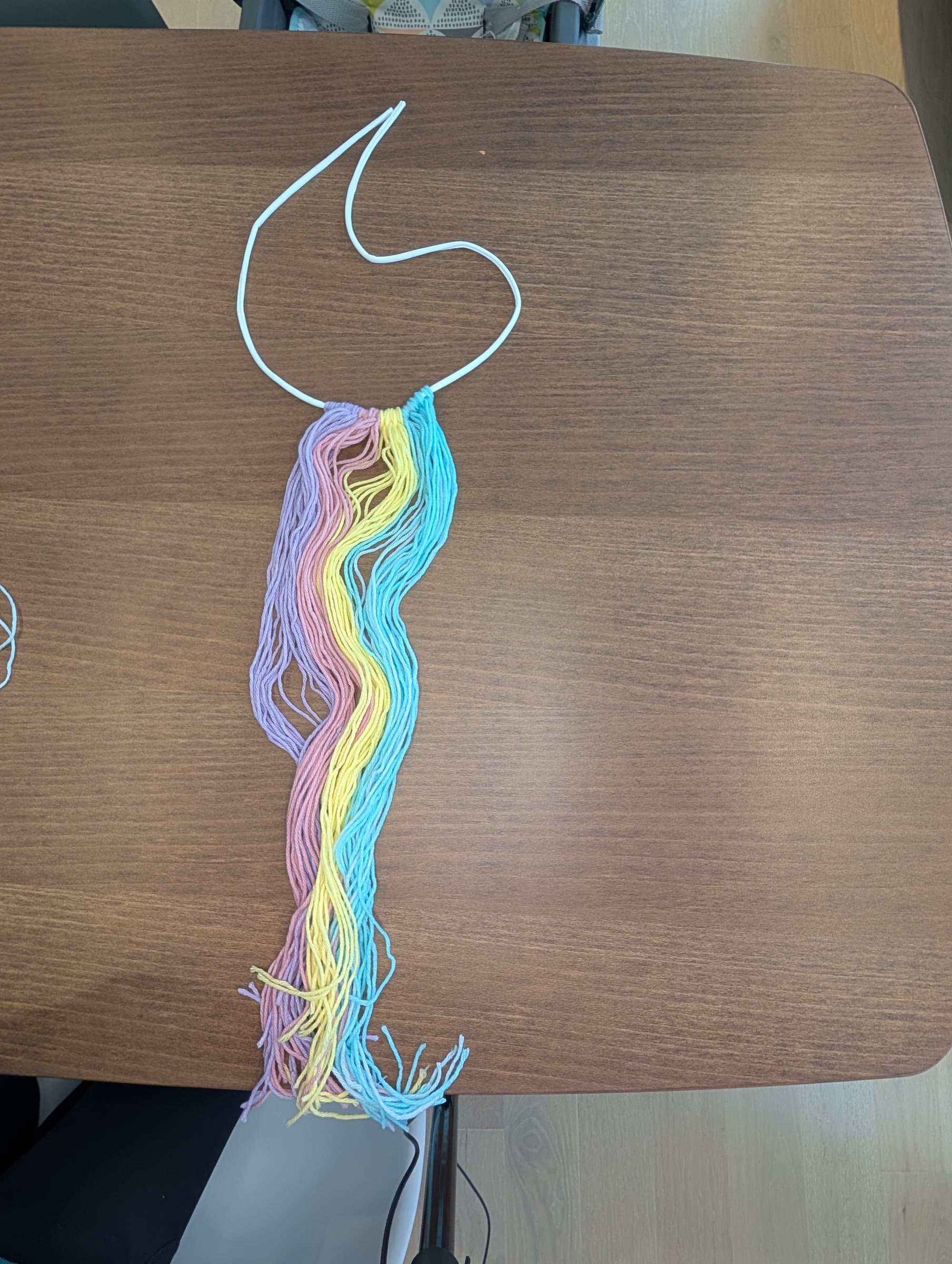Pastel purple, pink, yellow, and blue yarn strips looped onto a white elastic cord, before braiding