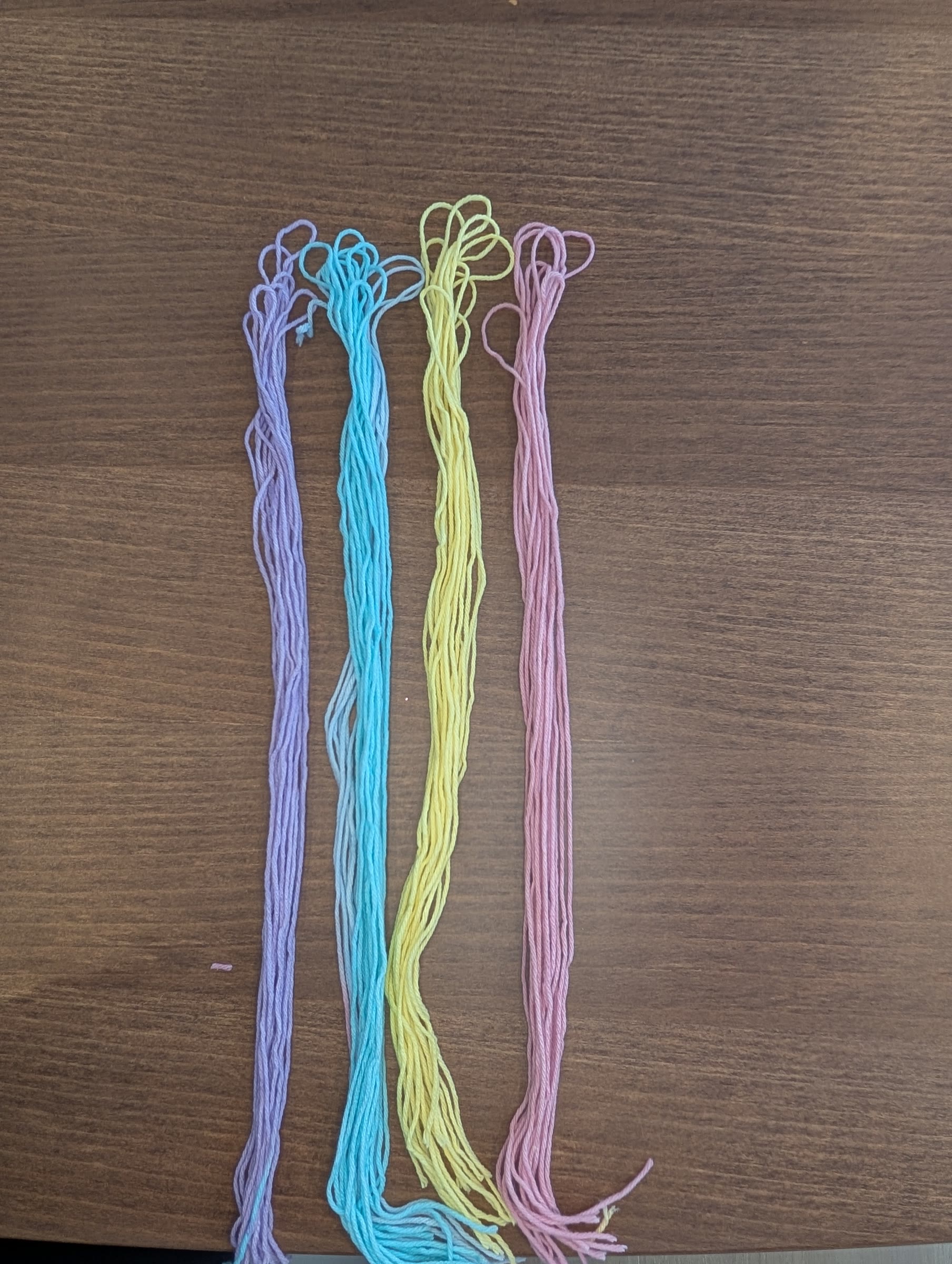 Four bundles of pastel yarn strips laid side by side: purple, blue, yellow, and pink